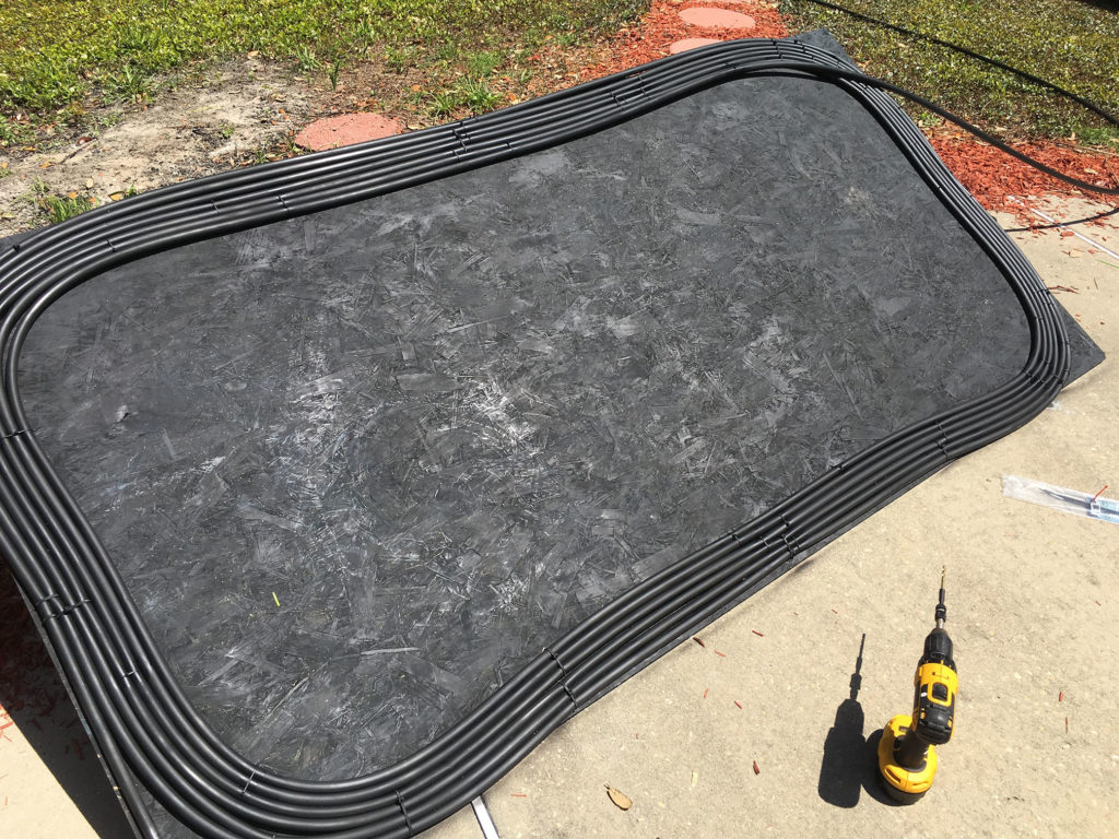 Close-up of black hose routing and zip ties securing the coil to plywood